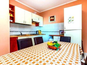 A compact kitchen with white cabinets, a tiled backsplash, and a dining table with a checkered tablecloth. - Wohnung in Novi Vinodolski mit Grill, Garten und by Interhome (Novi Vinodolski)