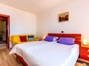 Een slaapkamer met een bed, een nachtkastje, een schilderij en een deur naar een andere kamer.