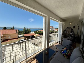 A balcony with a view of the sea and buildings, a table with a chair, and a hanging chair. - Apartment Val by Interhome (Crikvenica)