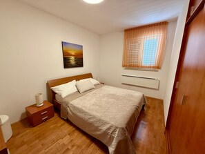 Una camera da letto con un letto di legno, un comodino, una lampada da comodino, una finestra con persiane e un quadro appeso al muro.