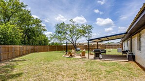 Een achtertuin met een overdekte patio, een barbecue en buitenmeubilair.