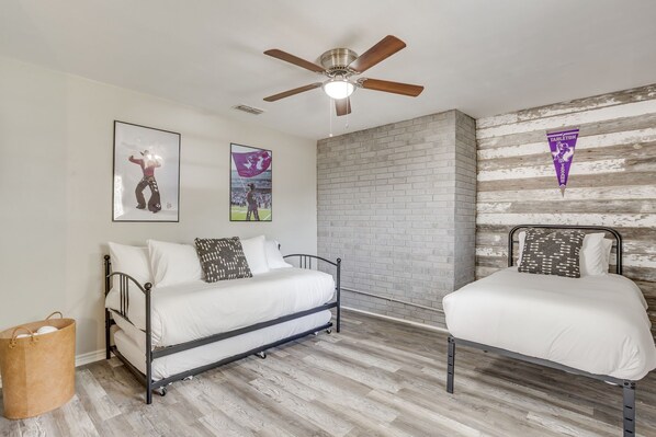 A bedroom with two beds, a ceiling fan, and a brick wall.