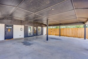 A covered parking area with a concrete floor, a wooden fence, and a brick wall.