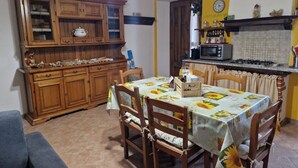 A dining area with a table set for four, surrounded by wooden chairs. A kitchen with a stove and microwave is visible in the background. - Relaxing Home with a View of the Sea (Toscana)