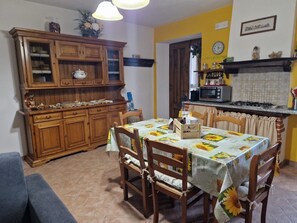 A dining area with a table set for four, surrounded by wooden chairs. A kitchen with a stove and microwave is visible in the background. - Relaxing Home with a View of the Sea (Toscana)