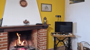 A room with a brick fireplace, a television on a table, and a painting on the wall. - Relaxing Home with a View of the Sea (Toscana)