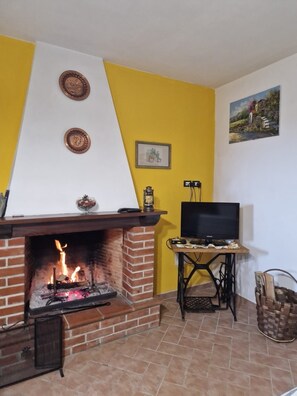 A room with a brick fireplace, a television on a table, and a painting on the wall. - Relaxing Home with a View of the Sea (Toscana)