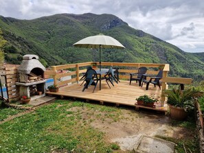 An outdoor patio with a wooden deck, a stone oven, and a table with chairs. - Relaxing Home with a View of the Sea (Toscana)
