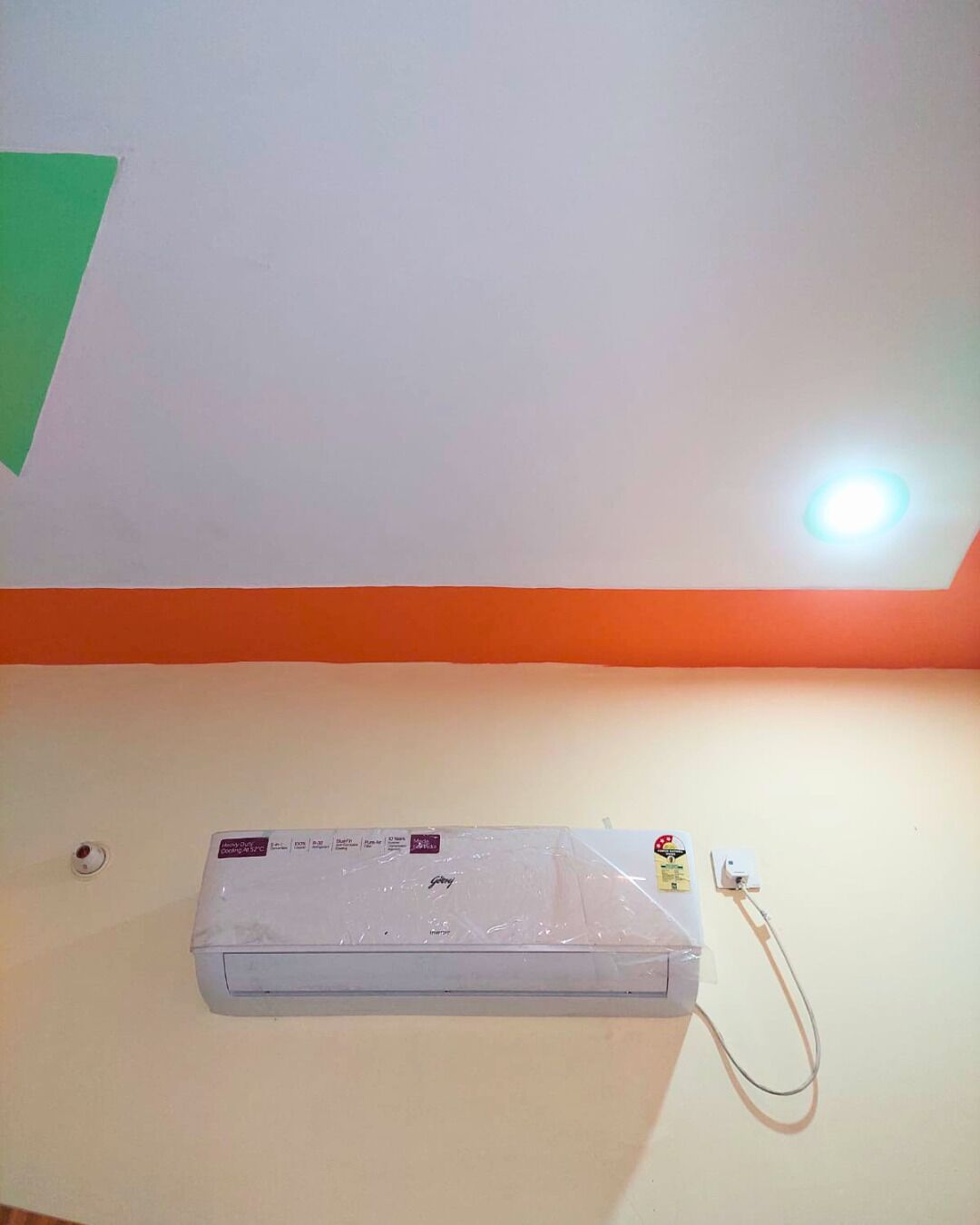 Ein Zimmer mit weißer Decke, einer grünen, dreieckigen Dekoration und einer weißen Klimaanlage an der Wand.