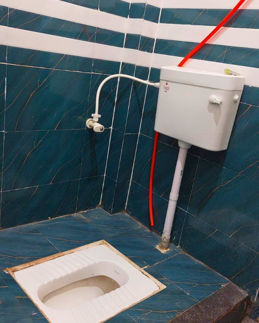 A small bathroom with a toilet, a white tank, and a blue tiled wall.