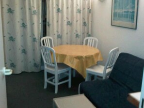 Ett rum med ett runt bord, två stolar, en soffa och ett fönster med gardiner.