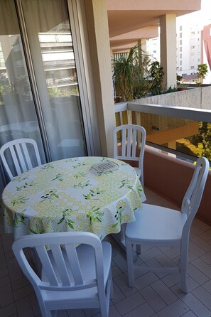 Ein Balkon mit einem runden Tisch und vier weißen Stühlen, bedeckt mit einer blumigen Tischdecke.