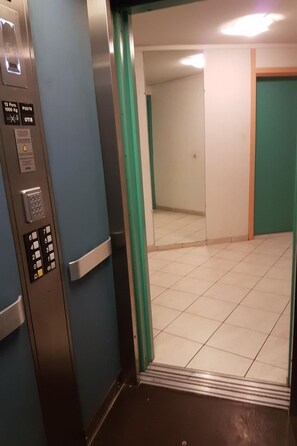 En hissinredning med en manöverpanel, instruktioner för nödsituationer och ett kaklat golv.