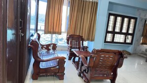 A room with a wooden sofa set, a dining table, and a window with curtains. - Hotel Jayalakshmi Residency (Tirupati)