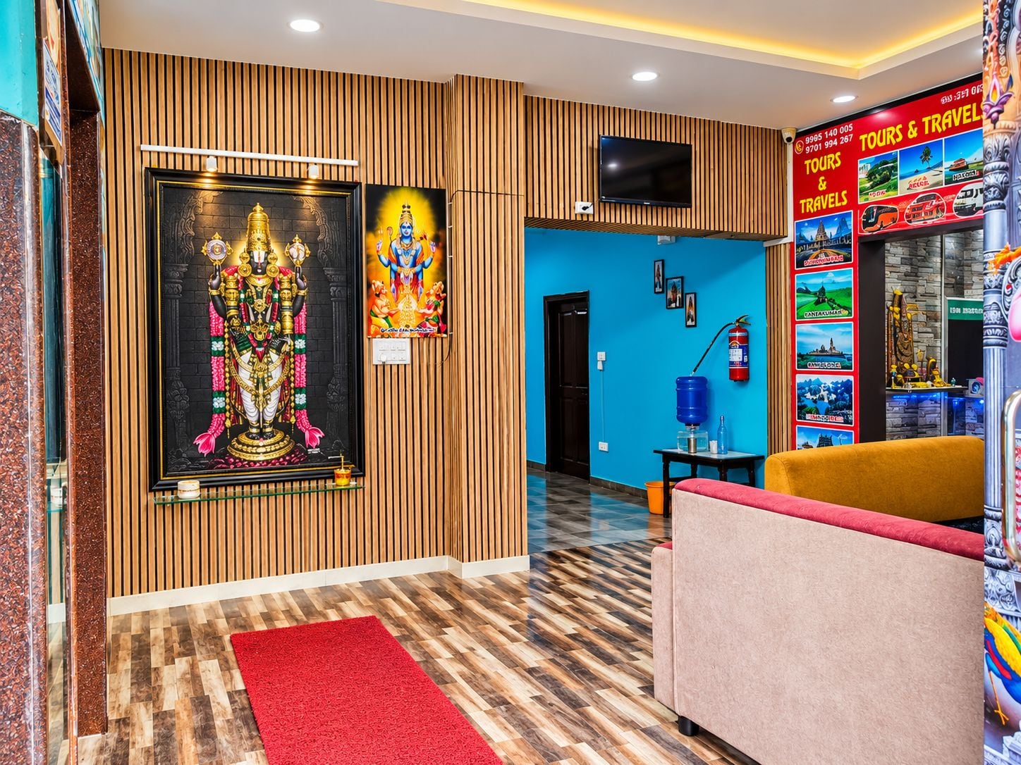 Un vestíbulo de hotel con un panel de madera decorativo, un cuadro religioso enmarcado, un televisor y un tablón de información turística.