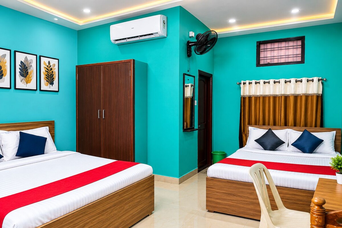 Habitación de hotel con dos camas, un armario, aire acondicionado, ventilador, ventana con cortinas y una pequeña mesa con una silla.