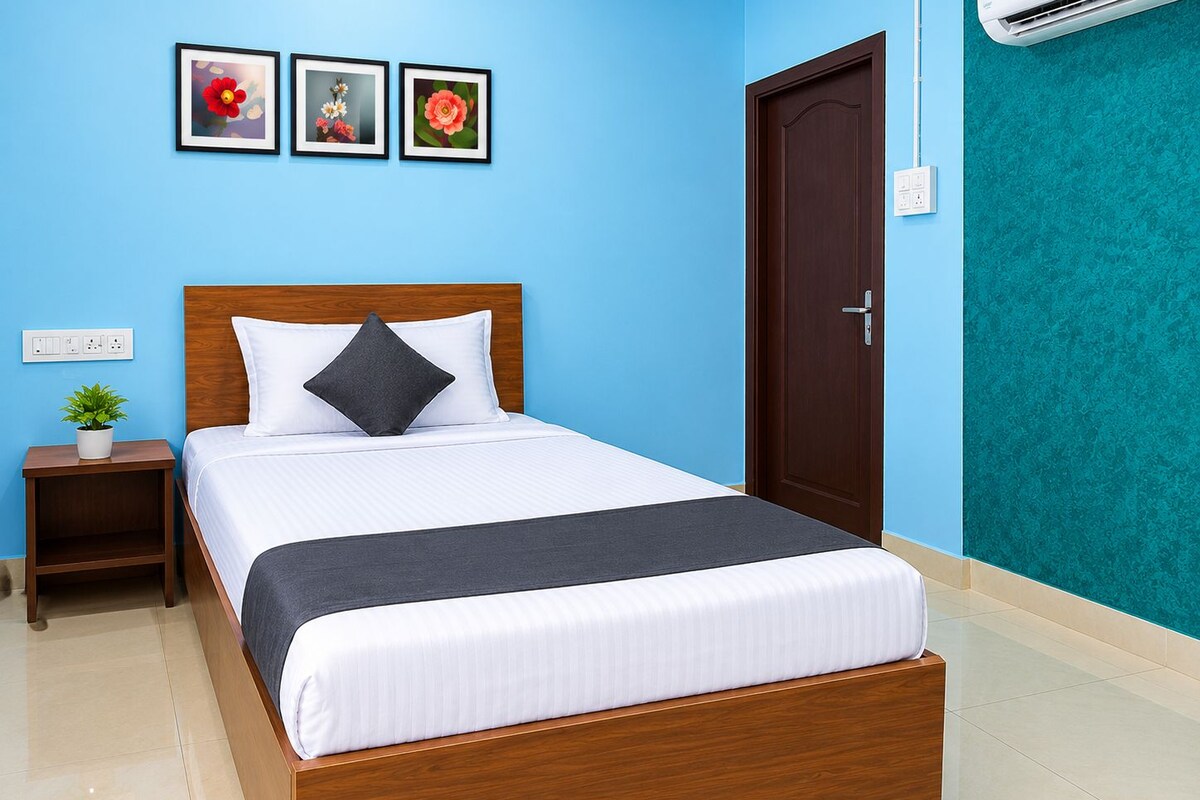 Una cama bien tendida con cabecera de madera, una mesita de noche con una planta y tres cuadros florales en la pared.