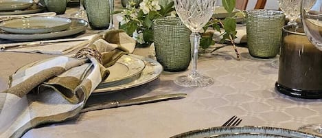 A dining table set with plates, glasses, and cutlery, with a kitchen in the background.