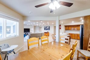 A spacious dining area with a wooden table and chairs, a ceiling fan, and a view into a living room with a sofa and television. - Las Palmas 1605 | Next to Clubhouse and Pool! (Saint George)