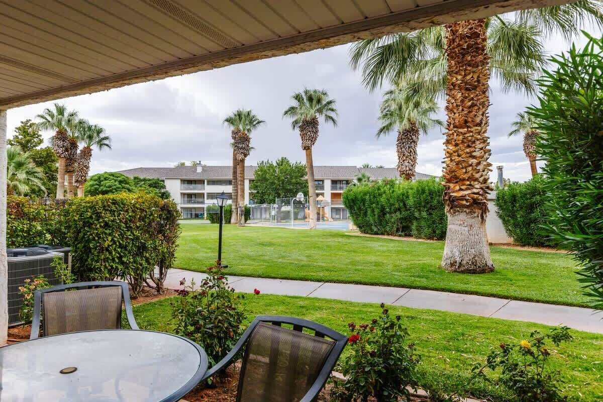 An outdoor patio area with a table and chairs, surrounded by palm trees and a well-maintained lawn.