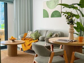 Ett modernt vardagsrum med en grå soffa, två runda träbord och en stor krukväxt.