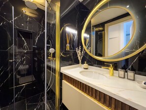 Ein Badezimmer mit Marmorwaschtisch, goldenen Armaturen und einem großen Spiegel.