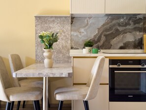 Una cocina moderna con salpicadero de mármol, horno empotrado y comedor con sillas y un jarrón de flores.