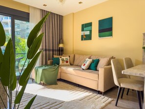 A modern living room with a sofa, a dining table, and chairs. There is a large window with curtains, a plant, and artwork on the wall. - Qoople Legend 36 A-04 100 Meter vom Strand entfernt by Interhome (Alanya)