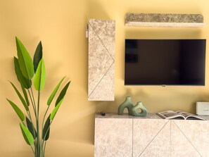 A modern living room with a flat-screen TV mounted on the wall, a marble-patterned cabinet below, and a potted plant on the left. - Qoople Legend 36 A-04 100 Meter vom Strand entfernt by Interhome (Alanya)