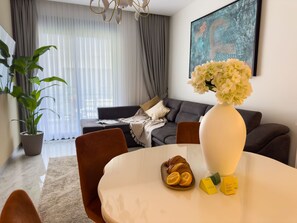 Ein modernes Wohnzimmer mit Esstisch, Stühlen, einer Couch, einer Zimmerpflanze und einer Vase mit Blumen.