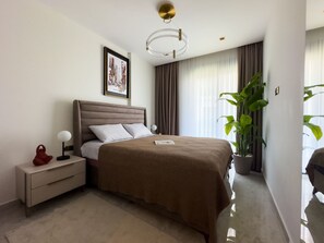 Ein modernes Hotelzimmer mit einem großen Bett, einem Nachttisch, einer Lampe, einem gerahmten Bild an der Wand und einer Topfpflanze.