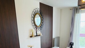 A dining area with a white table set for four, a potted plant, and a mirror on the wall. - SADAM NEST PRIVATE (Le Mans)