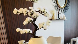 A dining table set with white floral plates, a vase with white flowers, and a mirror on the wall.