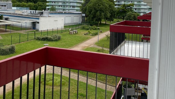A balcony with a red railing overlooking a courtyard with buildings and trees. - SADAM NEST PRIVATE (Le Mans)