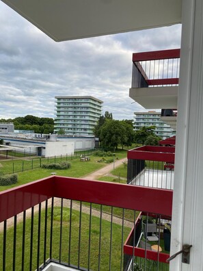 Un balcón con barandilla roja que da a un patio con edificios y árboles.
