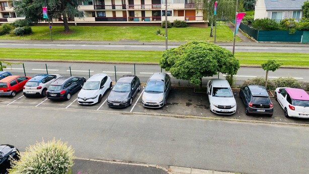 A parking lot with multiple cars, a building with balconies, and a grassy area in the background.