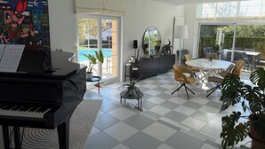 A modern living room with a piano, a dining area, and a view of a swimming pool. - Maison d’architecte lumineuse • Au cœur des Vosges (Deyvillers)