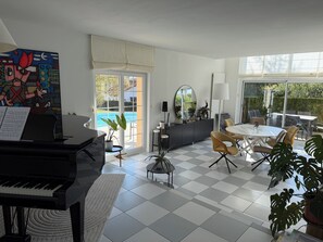Ein modernes Wohnzimmer mit Klavier, einem Essbereich und Blick auf einen Pool.