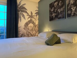 Ein Hotelzimmer mit einem Bett, einem Fenster mit Vorhängen und zwei an der Wand hängenden Bildern von Wildtieren.