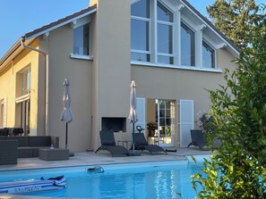 Ein modernes Gebäude mit einem Schwimmbad, Sitzgelegenheiten im Freien und einem Kamin.