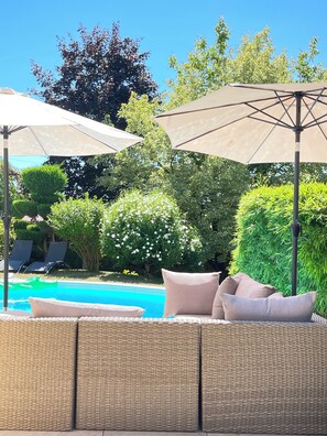 Un espace aménagé au bord de la piscine, avec des meubles en osier et des parasols.