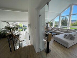 Un salon moderne avec une cloison en verre, un escalier, un canapé et une vue sur la verdure.