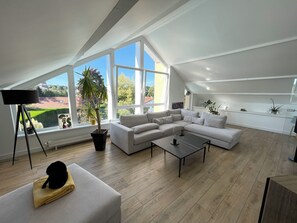 Ein modernes Wohnzimmer mit einem Ecksofa, einem Couchtisch und einem großen Fenster mit Blick auf einen Garten.