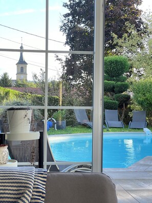 A pool area with a view of a church steeple, lounge chairs, and a potted plant. - Maison d’architecte lumineuse • Au cœur des Vosges (Deyvillers)