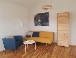 A modern living room with a sofa, chairs, a small table, a floor lamp, a painting, and a wooden wardrobe. - Vacation Rental Next to the Ceramics Studio (Babensham)