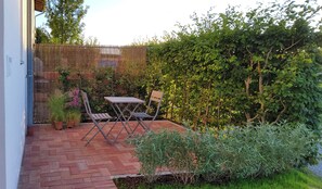 A patio with a table and chairs, surrounded by a bamboo fence and lush greenery. - Vacation Rental Next to the Ceramics Studio (Babensham)
