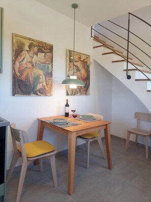 Un coin repas comprenant une table en bois, deux chaises, une suspension et deux tableaux accrochés au mur.