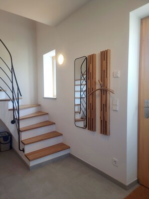 A staircase with wooden steps and a black metal railing, a wall-mounted mirror, and a light fixture. - Vacation Rental Next to the Ceramics Studio (Babensham)
