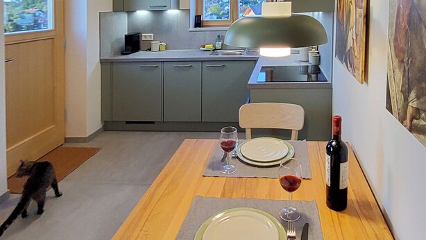 Een eetruimte met een tafel gedekt voor twee personen, een fles wijn en een schilderij aan de muur.