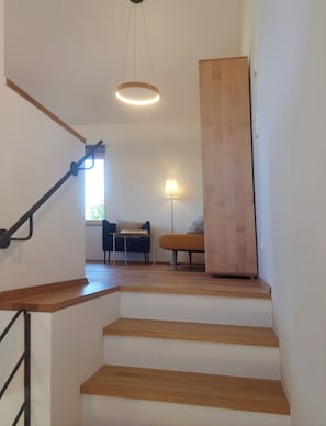 Un escalier avec des marches en bois menant à un palier. On aperçoit une lampe sur le palier et une chaise au fond.